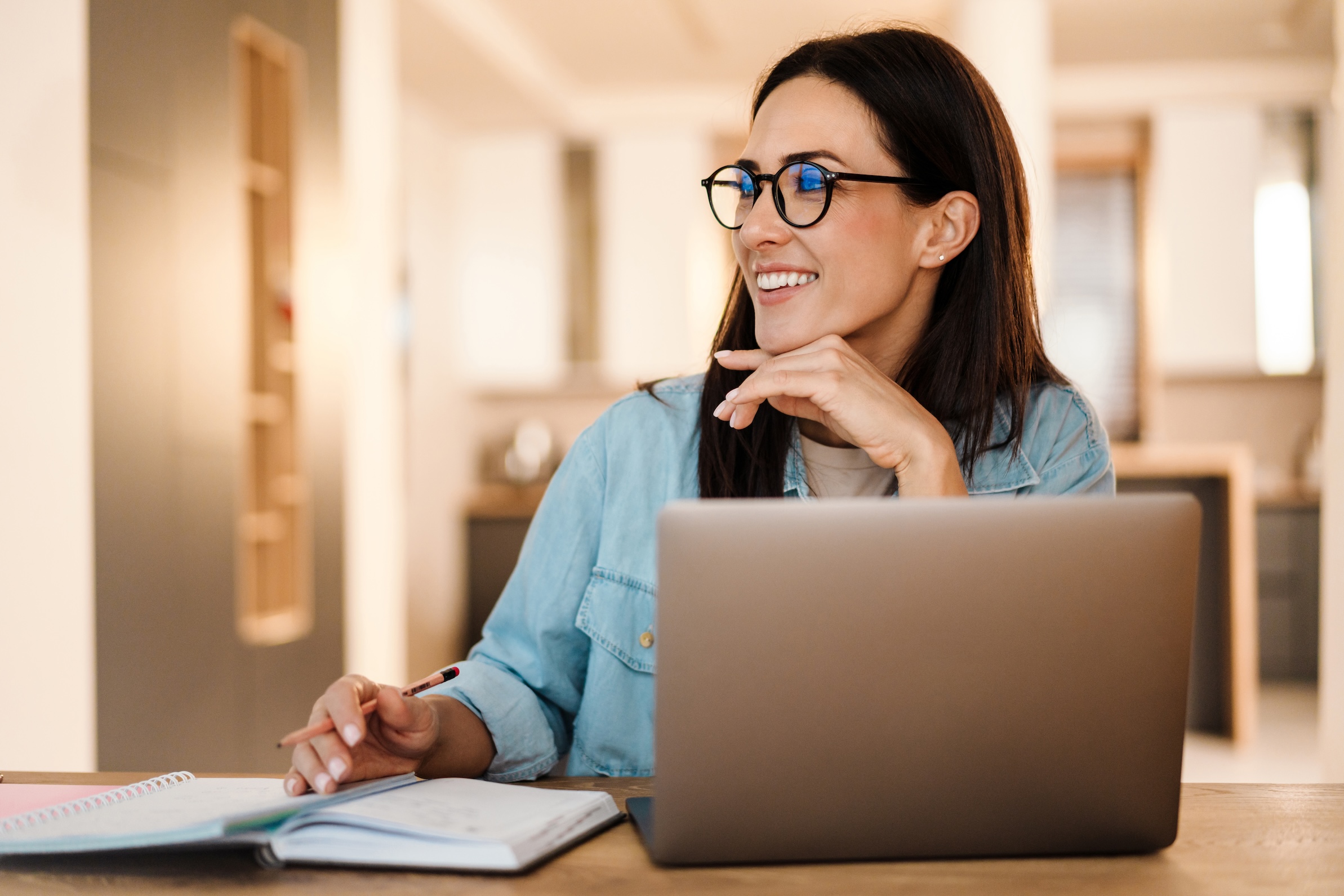 Happy charming woman writing down notes while working with laptop